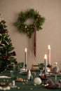 Interior design of warm dining room with table, wreath, christmas tree, green tablecloth, stylish chair, glasses candle with Royalty Free Stock Photo