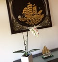 Interior Design. On the wooden table was a pot of orchids and a boat ornament and the wall hung a wooden frame with a gold