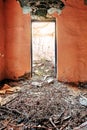 Interior of a desolated old rural house with light pink cracked walls, detached door and a floor covered with mud