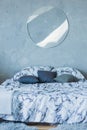 Interior: double bed with pillows and a lamp in the form of a circle on a gray wall.