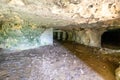 Interior of an empty cave, walls with uneven texture and cracks, concrete supports or columns in background