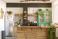 Interior home decoration. Beautiful and open bright kitchen with wooden kitchen island, green cabinet, big windows and plants.