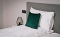 A dark green turquoise pillow on white sheets on a bed.