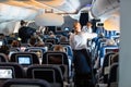 Interior of large commercial airplane with stewardesses serving passengers on seats during flight. Royalty Free Stock Photo