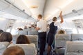 Interior of large commercial airplane with stewardesses serving passengers on seats during flight. Royalty Free Stock Photo