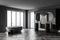 Interior of modern bathroom with dark gery wooden walls, concrete floor, two sinks with two round mirrors above it and comfortable