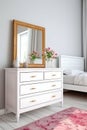 Interior of modern bedroom with wooden chest of drawers and mirror.