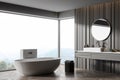 Interior of modern corner bathroom with dark brown walls  wooden floor  white bathtub and double sink with round mirror. Royalty Free Stock Photo