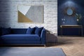 The interior of a modern living room with a dark blue sofa next to a brick wall on which a horizontal poster hangs. Royalty Free Stock Photo