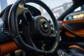 An interior of a modern McLaren supercar with a luxurious black leather steering wheel