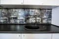 Interior of modern spacious kitchen with white contemporary furniture, black ceramic tiles on the wall and dark granite sink with Royalty Free Stock Photo