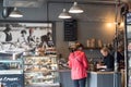 Interior of modern trendy cafe with cake display and female customer being served a hot drink