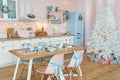 Interior of modern white kitchen with pink walls and blue decor on a Christmas New year eve. Pine tree with wrapped gifts and