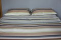 Interior natural light shot of a colorful, striped bed linen with two pillows, a duvet with textile cotton sheets on a king size Royalty Free Stock Photo