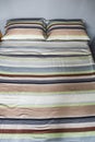 Interior natural light shot of a colorful, striped bed linen with two pillows, a duvet with textile cotton sheets on a king size Royalty Free Stock Photo