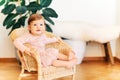 Interior portrait of adorable baby girl sitting on wicker chair Royalty Free Stock Photo