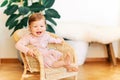 Interior portrait of adorable baby girl sitting on wicker chair Royalty Free Stock Photo