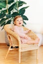 Interior portrait of adorable baby girl sitting on wicker chair Royalty Free Stock Photo