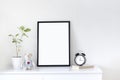 Interior poster mock up with vertical black frame, plant in a pot, bear toy, book and clock on a white table and white