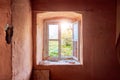 Interior of a ruined old cottage with a light pink wall and a broken wooden window frame viewing a rural green meadow field Royalty Free Stock Photo