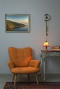 Interior shot of retro orange armchair, vintage wooden beige table, illuminated antique table lamp, old books, and pendulum clock Royalty Free Stock Photo