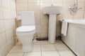 Interior of simple half bathroom with toilet, sink and bath with shower, white sanitary ware