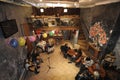 Interior of small art cafe Tarelka - Plate-, girls musicians on stage ready to play, visitors sitting at tables. Kyiv