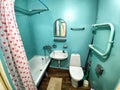 The interior of a small, modest bathroom with a bath and a toilet. Green walls, curtains with a red dot. The concept of