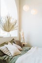 Interior of sunny modern bedroom with bed covered with grey bed linen, beige plaid. Different glass vase with dry plant.