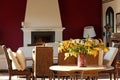 Interior with table and flowers in vase, chairs and dining table, fireplace. The room painted by dark red violet color