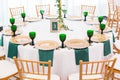 Interior of tent for wedding dinner, ready for guests. Served round banquet table. Golden dishes, green wine glasses and Royalty Free Stock Photo