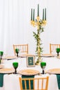 Interior of tent for wedding dinner, ready for guests. Served round banquet table. Golden dishes, green wine glasses and Royalty Free Stock Photo