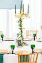 Interior of tent for wedding dinner, ready for guests. Served round banquet table. Golden dishes, green wine glasses and Royalty Free Stock Photo