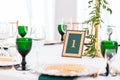 Interior of tent for wedding dinner, ready for guests. Served round banquet table. Golden dishes, green wine glasses and Royalty Free Stock Photo