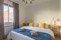 Interior of touristic bedroom with window. Yellow pillows on bed with towels. An apartment ready for booking by tourists