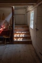 Interior of a very old fishing shack, light streaming through window onto stairs, table and chair