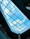 Interior view of a modern atrium skylight with geometric grid framing a bright blue sky and clouds. Clean architectural design. Royalty Free Stock Photo