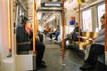 Interior view of a subway train with several passengers seated and reading