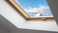 Interior view of a white attic window with wooden frame looking out at snowy rooftops under a cloudy blue sky Royalty Free Stock Photo