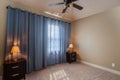 Interiors of a bedroom of a house with blue curtains, side shelves, lamps, white walls and carpet