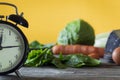 Intermittent fasting, clock with vegetables around and yellow background