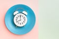 Intermittent fasting concept. White alarm clock on empty blue plate. Top view, copy space