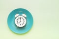 Intermittent fasting concept. White alarm clock on empty green plate. Top view, copy space
