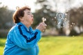 International Day of Older Persons. Portrait of an elderly caucasian grandmother blowing on a dandelion. Park in the