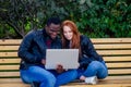 International education concept.dark skinned man wuth redhaired ginger woman looking at laptop and sitting on bench