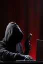 International hacker in black pullover and black mask trying to hack government on a black and red background. Cyber crime .