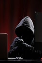 International hacker in black pullover and black mask trying to hack government on a black and red background. Cyber crime .