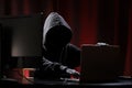 International hacker in black pullover and black mask trying to hack government on a black and red background. Cyber crime .