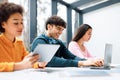 International students sitting in auditorium, focus on smiling guy using laptop, preparing for exam with classmates Royalty Free Stock Photo