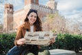 International tourist woman searching a location on a map. Happy female traveler smiling and looking at camera holding a